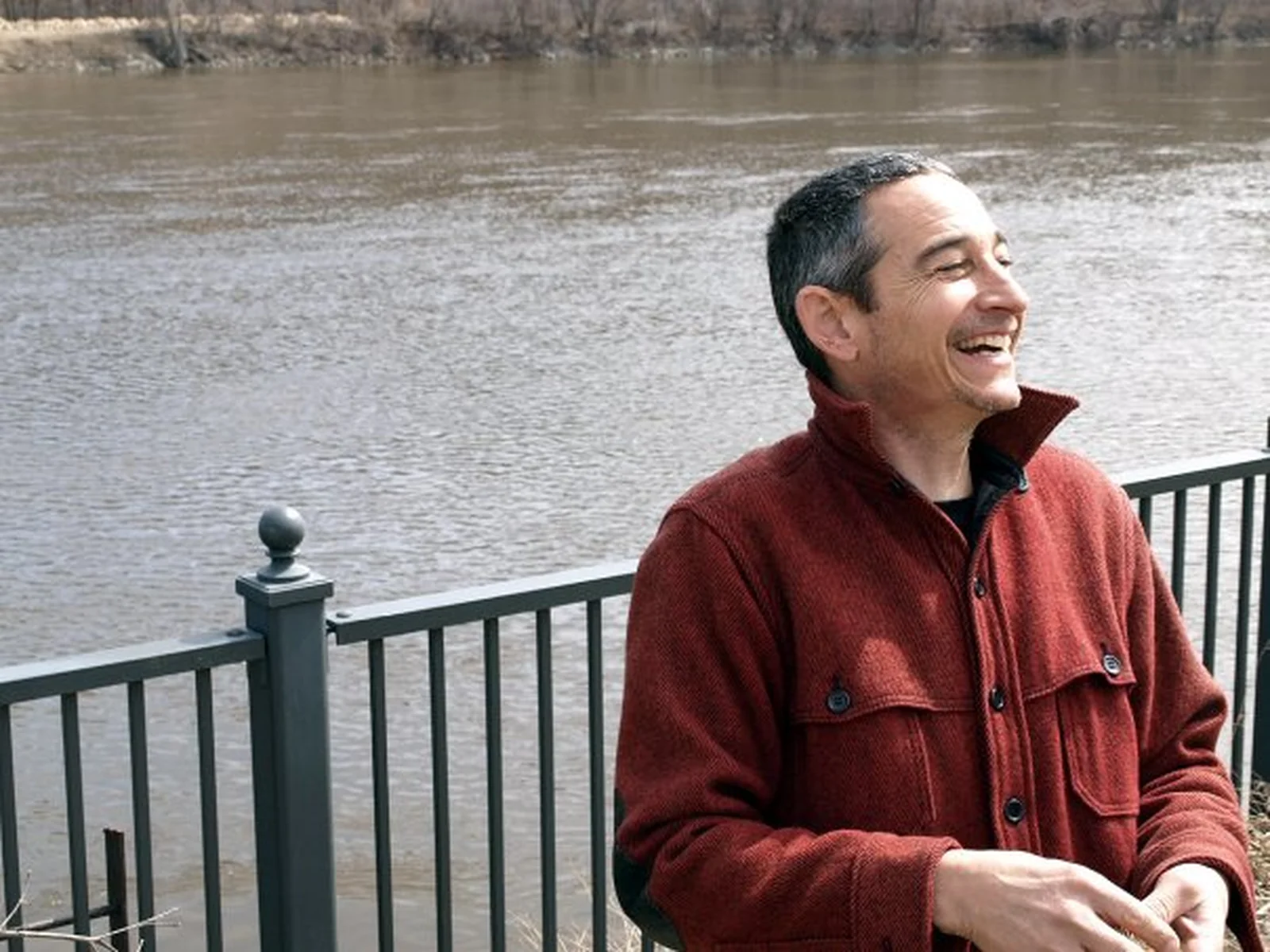 A person in a red jacket smiling by a river.