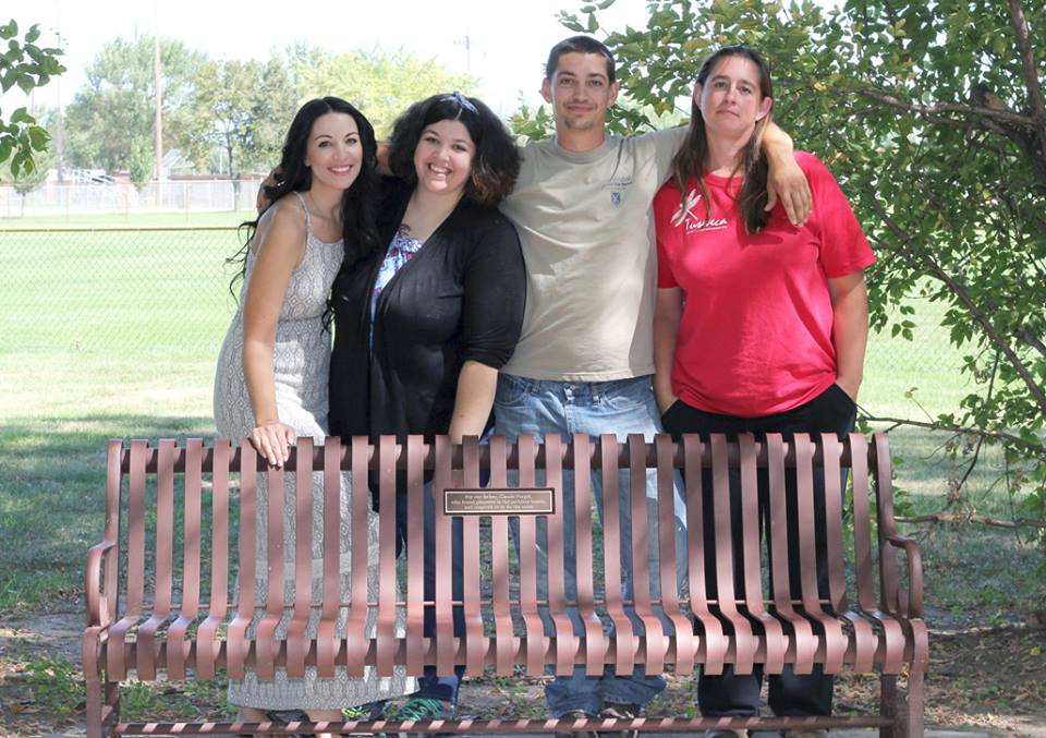 Nicole Arellano-Forget and her family standing behind the memorial bench placed for her father, Claude Forget, in a Greeley park.